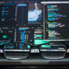 A pair of glasses resting on an open laptop with code in the background